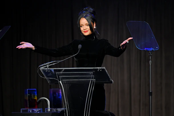 Rihanna stands at a podium with hands spread wide to the audience