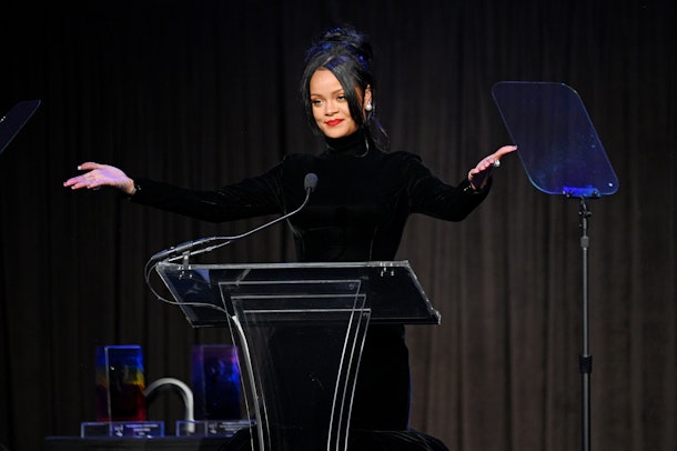 Rihanna stands at a podium with hands spread wide to the audience