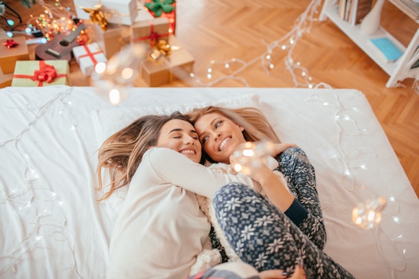 A lesbian couple lays in bed amongst twinkly lights and snuggles for a picture.