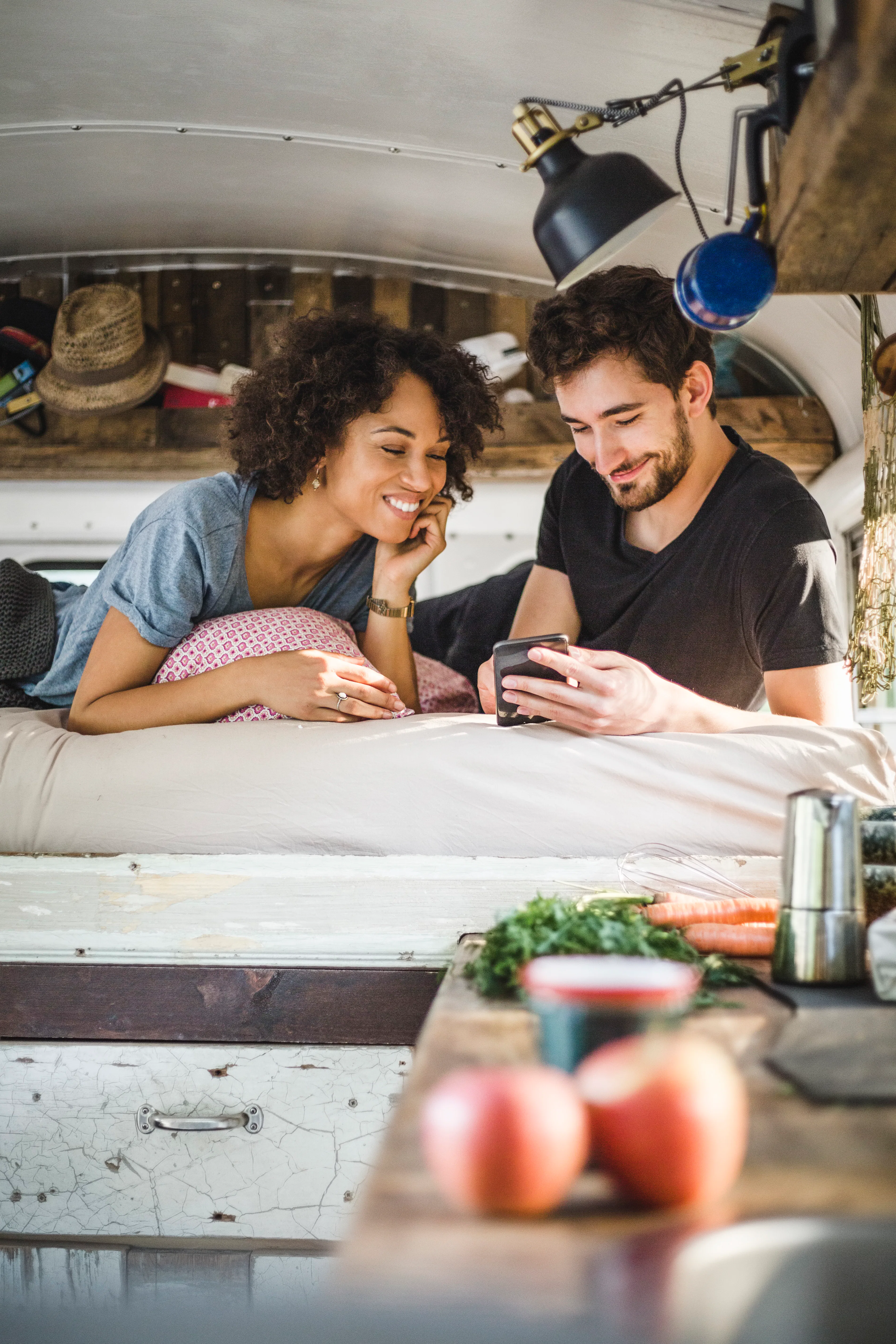 A young couple relaxes in a camper van while on a road trip, and looks at their phone.