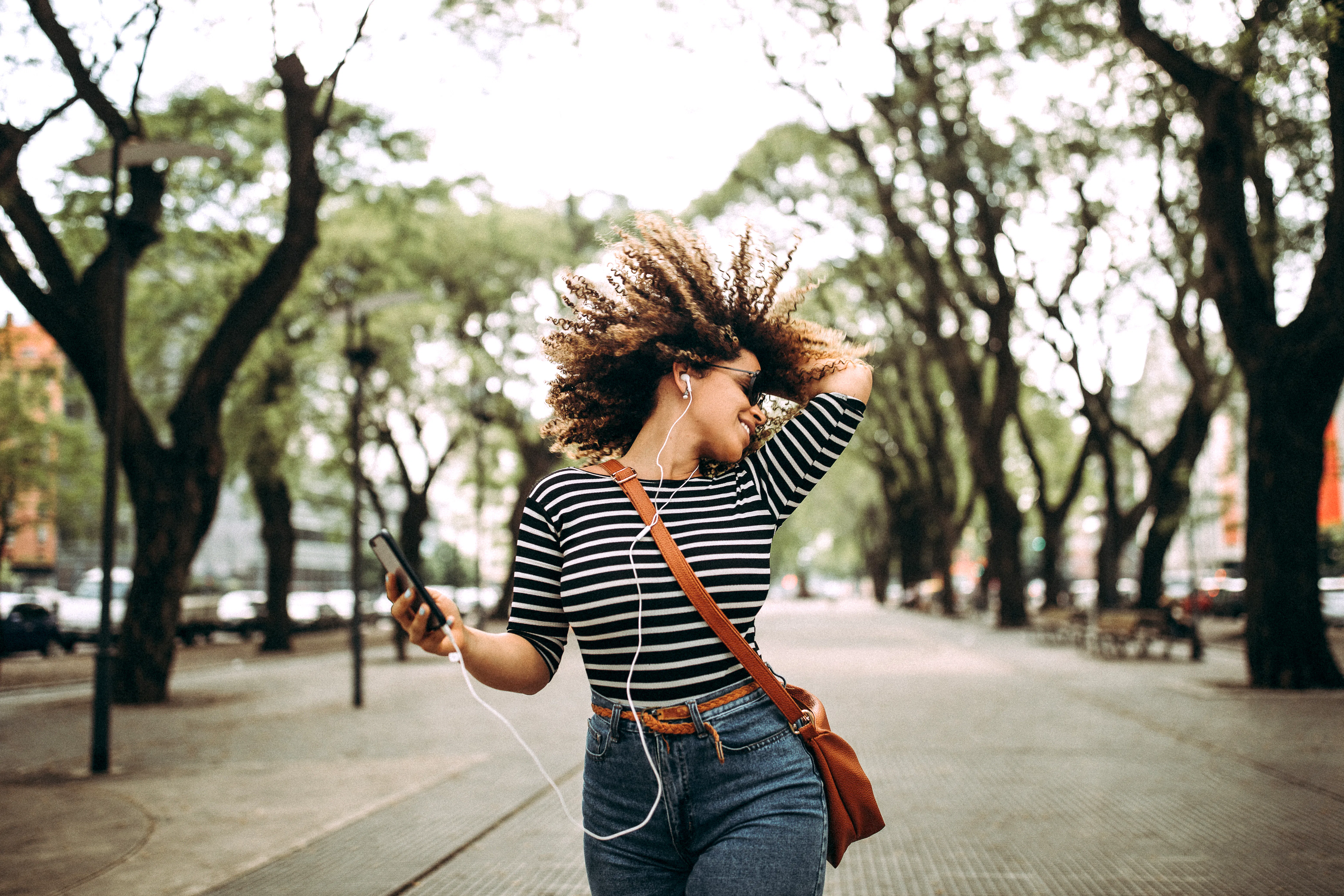 A happy woman dancing outside with her phone. 
