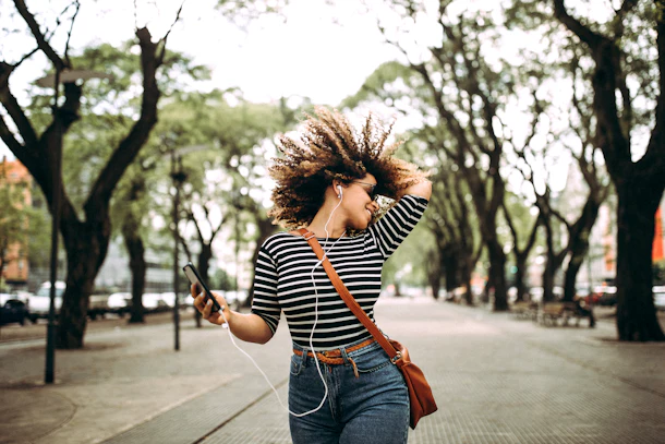 A happy woman dancing outside with her phone.