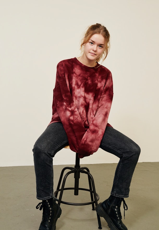 A young woman poses on a stool while wearing a tie-dye crewneck sweatshirt, black jeans, and combat boots for fall.