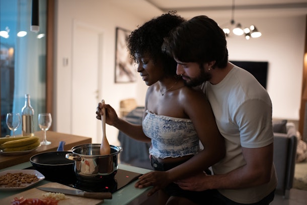 A couple works together to cooking something in the kitchen. 