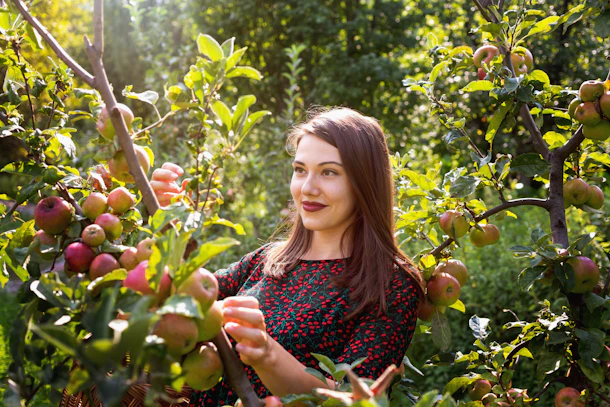 A woman in an apple orchard smiles on a sunny day.