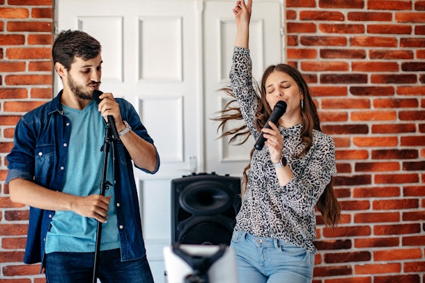 Two friends enjoy a round of karaoke in a trendy space with exposed brick.
