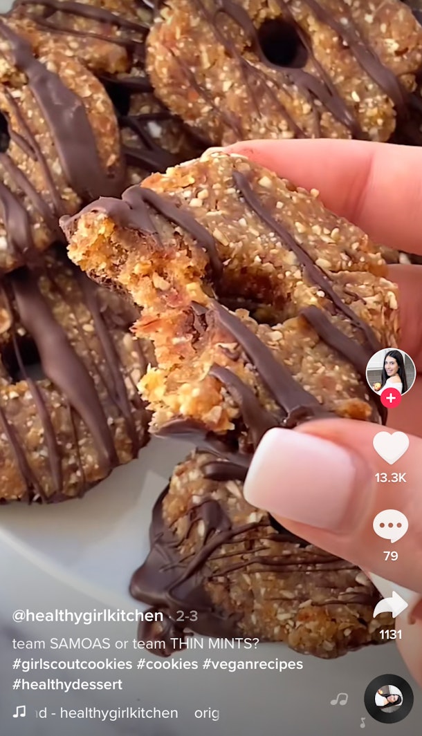 A woman holds up a vegan Samoa Girl Scout cookie. 