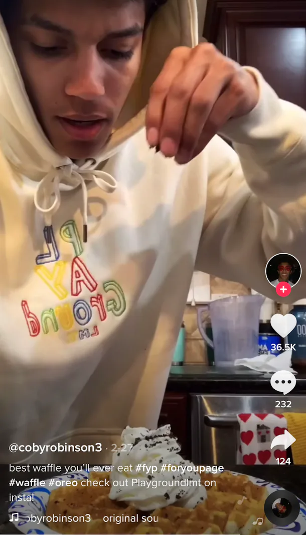 A man sprinkles on some crushed up Oreos to an Oreo waffle he made in his kitchen. 