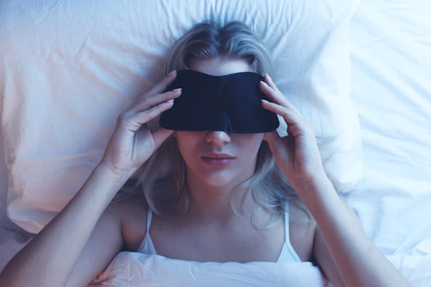 Sleeping girl in a sleep mask on an orthopedic pillow with night lighting, white bed linen.