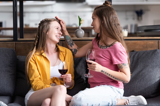 two lesbians holding wine glasses and looking at each other while sitting on sofa in living room