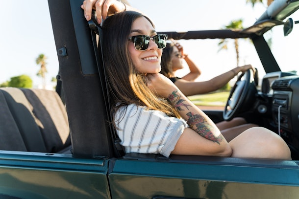 Happy Hispanic woman traveling with friend in 4x4 during summer