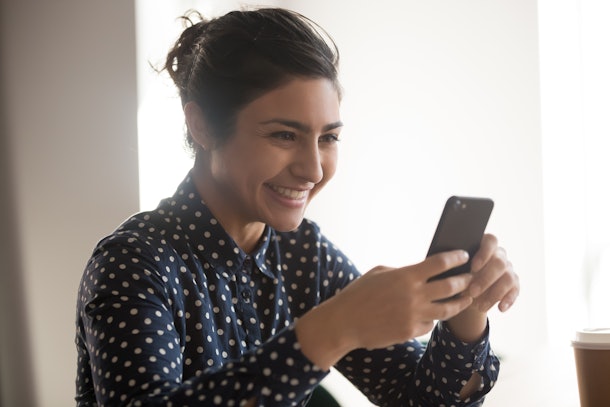 Close up of happy female indian employee holding smartphone texting message to friend, smiling ethnic woman having pleasant chat or conversation on cellphone, laughing watching funny video online
