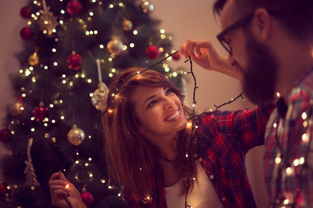 Beautiful young couple in love decorating Christmas tree, arranging the christmas lights and having fun