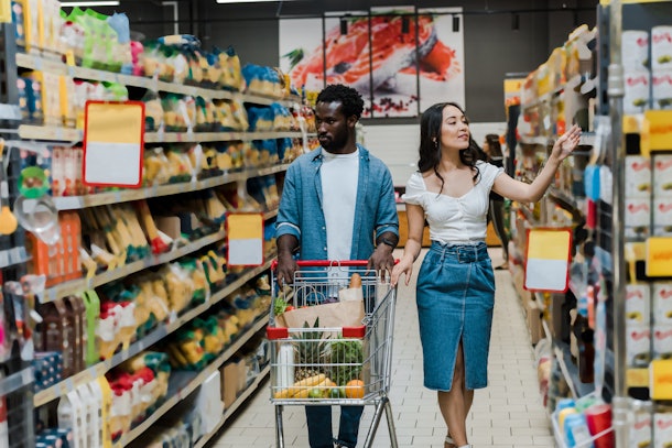 handsome man walking with shopping cart near attractive asian girl gesturing in store