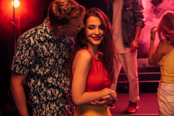 man kissing on cheek young woman during rave party in nightclub