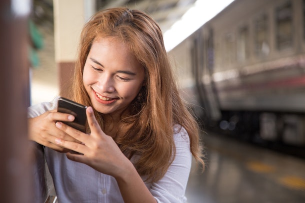 Young woman chating or messaging while using her mobile phone or her smart phone during her travelling or waiting the train in the train station