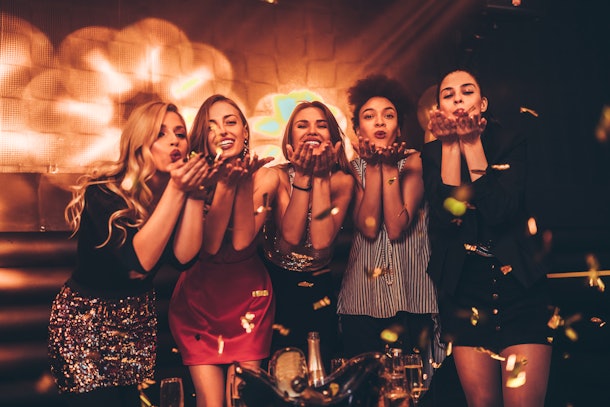 A group of women blow gold confetti into the air at a bar on New Year's Eve.