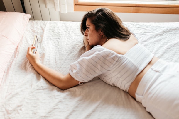 Portrait of young sad woman lying on the bed looking smartphone feels unhappy. Waiting for mobile message. Feeling worried, hurt, heartbroken lonely ignored by boyfriend not texting on cellphone