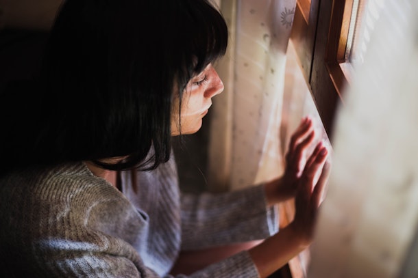 Portrait of a lovely sad lonely woman looking through the window the window waiting for somebody