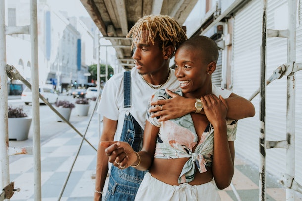 A happy couple stands on a sidewalk in a city.