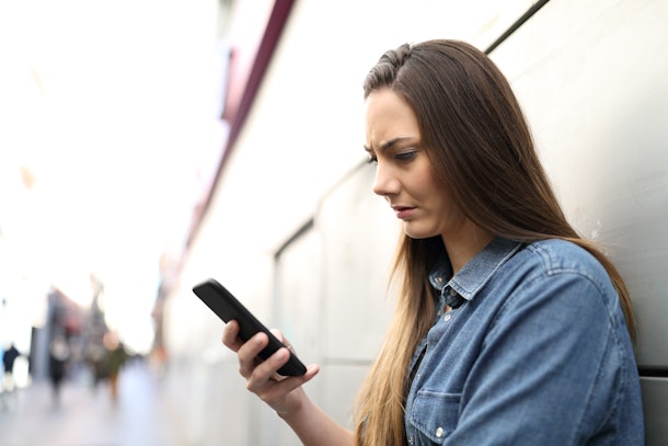 Profils of a sad woman checking smart phone online content in the street