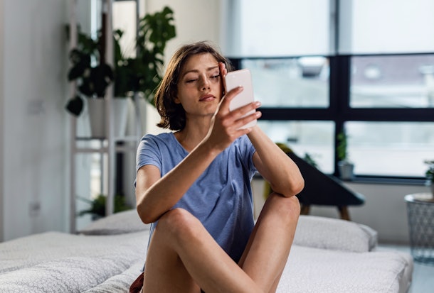 Unhappy woman reading bad news on cell phone and crying while sitting in the bedroom. 