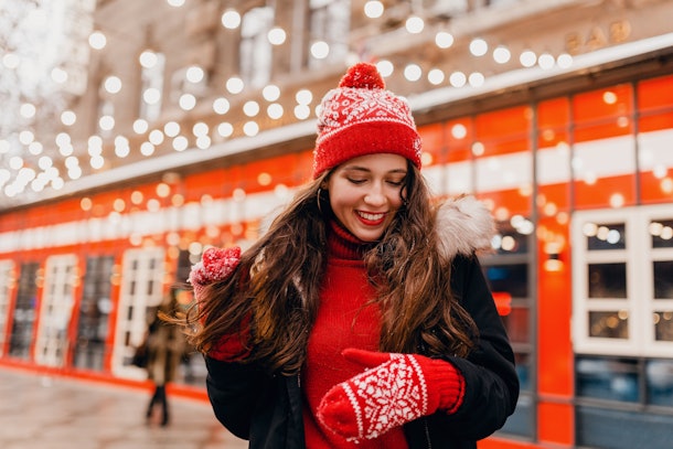young pretty smiling happy woman in red mittens and knitted hat wearing winter coat walking in city Christmas street, warm clothes style fashion trend