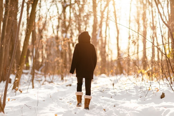 Winter snow walk woman walking away in snowy forest on woods trail outdoor lifestyle active people. Outside leisure.