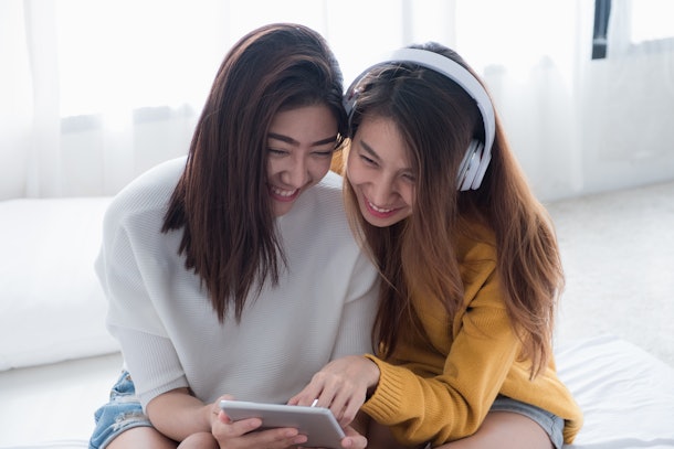 Two asia woman enjoy listening music app on tablet sitting on sofa in living room at home.Leisure digital lifestyle.Lesbian lgbt couple