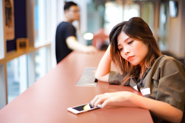 Lonely sad girl waiting for text message from smartphone on the table | Couple separated from each other