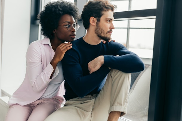 Sad disappointed european man can not forgive his african girlfriend infidelity, the girl is sitting next to man having apologetic guilty look, trying to make peace with man. Relationships problems