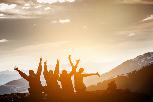 Group of friends sits on the top of mountain and having fun on mountains backdrop 