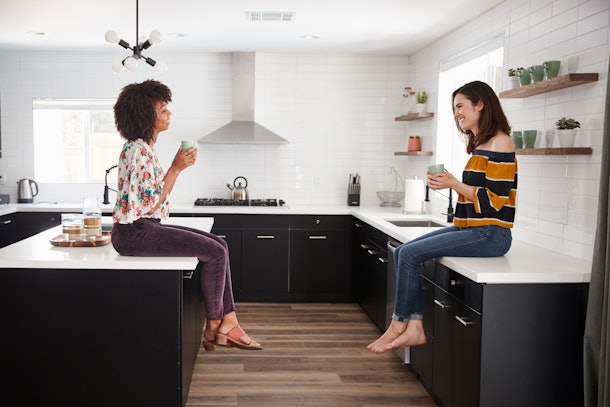 Two Female Friends Meeting For Coffee At Home Sitting On Kitchen Island