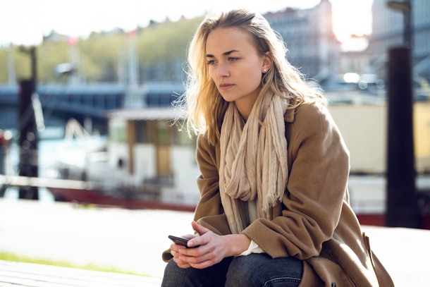 Shot of sad young woman thinking about her problems while sitting next to the river in the city.