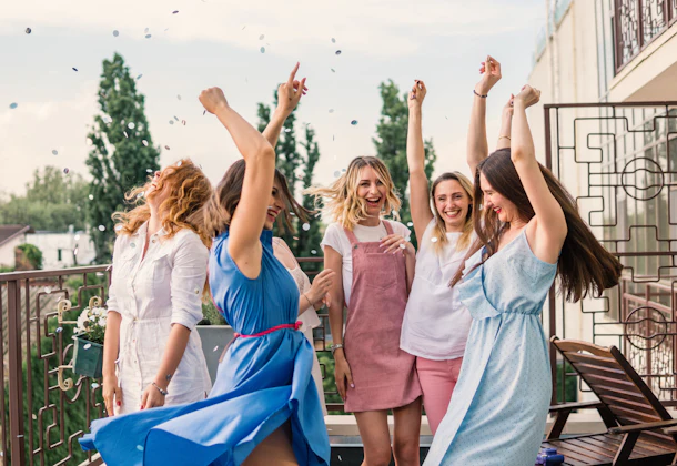 Girls Party. Beautiful Women Friends on the balcony Having Fun At Bachelorette Party. They are dancing in confetti with hands up