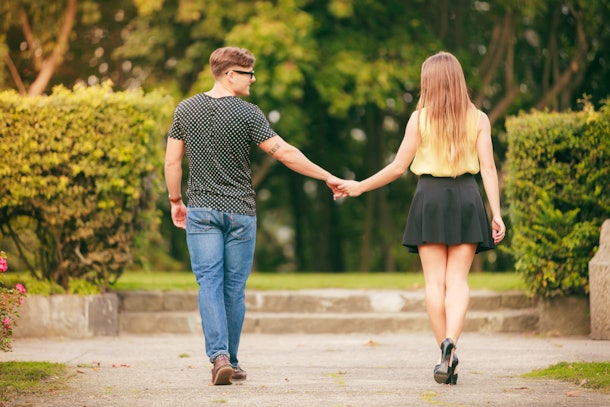 Dating. Young couple in love holding hands in summer park outdoor. Back view.
