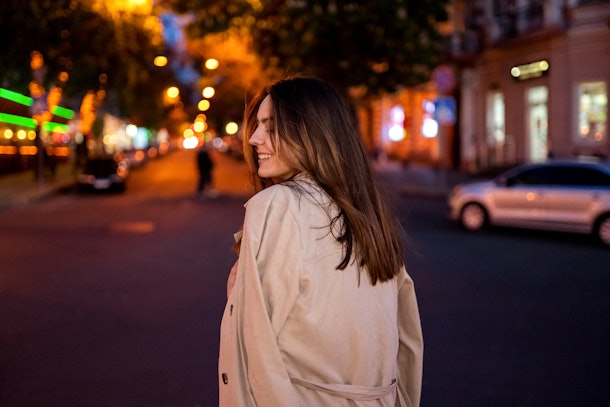 Beautiful brunette girl walks through the night city. Standing back. Awesome bokeh.