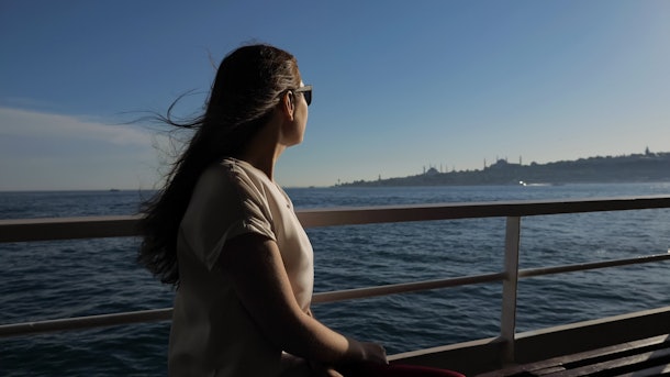 happy woman in sunglasses with waving hair travels by ship and enjoys magnificent seascape under sunshine closeup