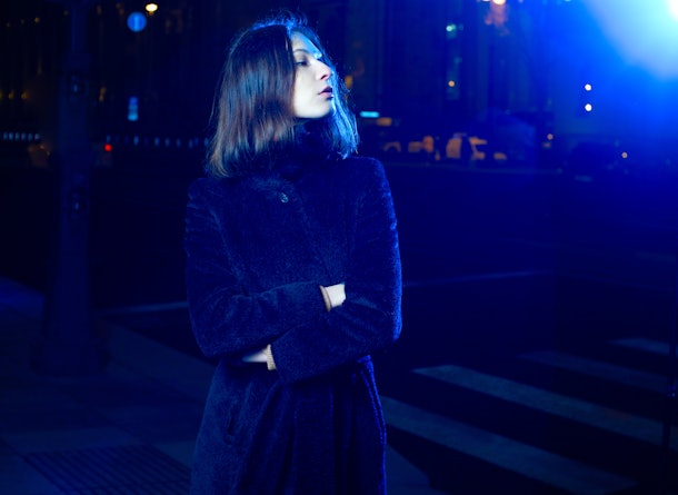 Fashion portrait girl in the night city and lights of street lamps. in the coat. illuminated by a blue lantern.