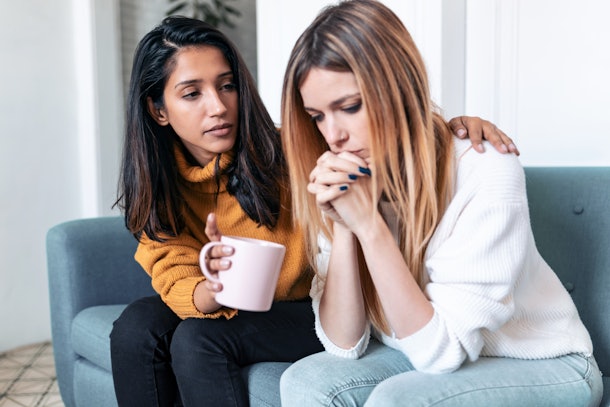 Shot of pretty young woman supporting and comforting her sad friend while sitting on the sofa at home.