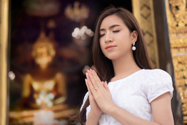 Religious Asian buddhist woman praying. Female buddhist disciple meditating, chanting mantra with prayer hand to the statue of lord Buddha in temple hall; concept of asian faith, belief, spirituality