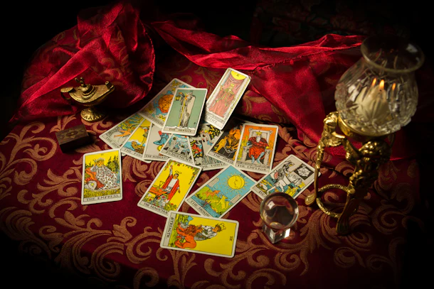 A pile of tarot cards lie scattered and spread across a table top surrounded by multiple occult items.