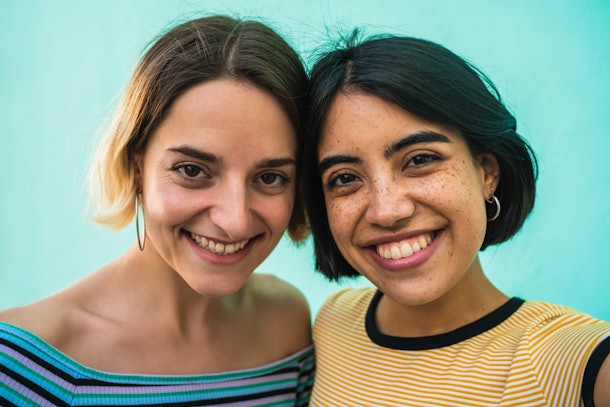 Portrait of lovely lesbian couple having fun and taking a selfie against light blue background. LGBT concept.