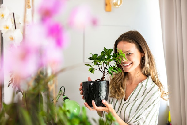 A happy woman holds up one of her potted plants at home.
